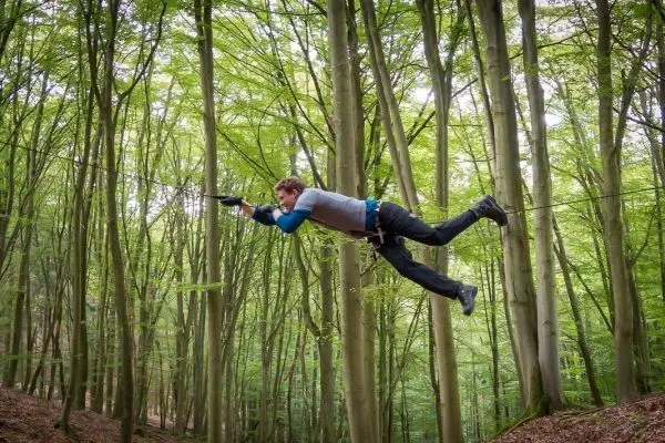 Mann überquert selbstgebaute Seilbrücke zwischen Bäumen im Wald