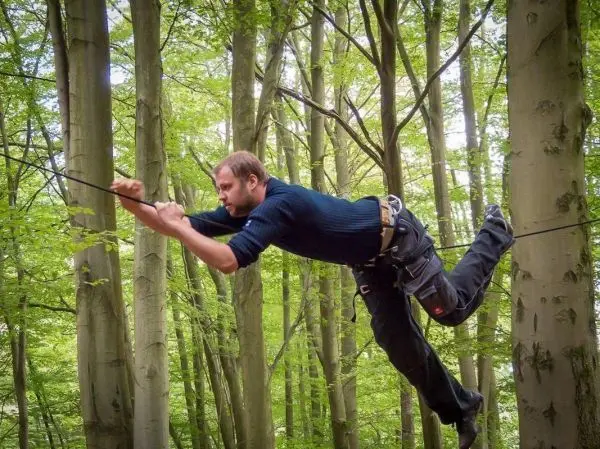Mann überquert selbstgebaute Seilbrücke zwischen Bäumen im Wald