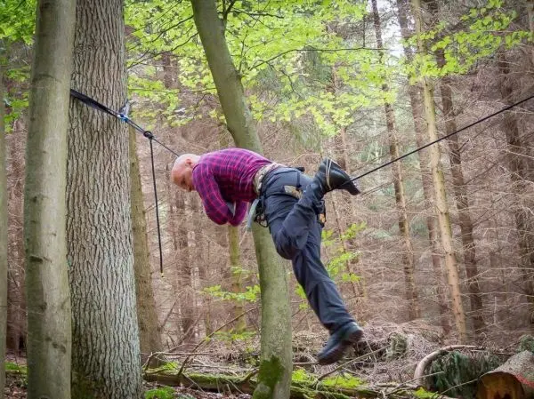 Mann überquert selbstgebaute Seilbrücke zwischen zwei Bäumen