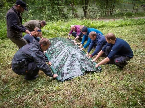 Mehrere Personen ziehen gemeinsam an einer Tarp-Notunterkunft auf dem Boden