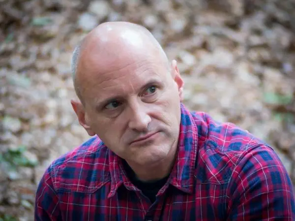 Nachdenklicher Mann in kariertem Hemd sitzt im Wald auf dem Boden