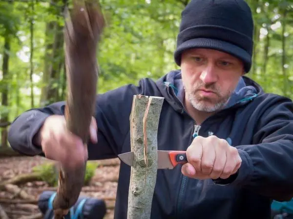 Person bearbeitet einen Stock mit einem Messer und einem Holzstück