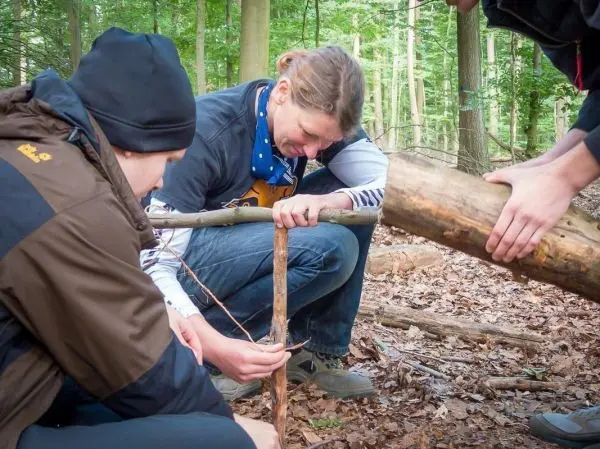 Person befestigt einen Stock mit Schnur an einem anderen Stock beim Überlebenstraining