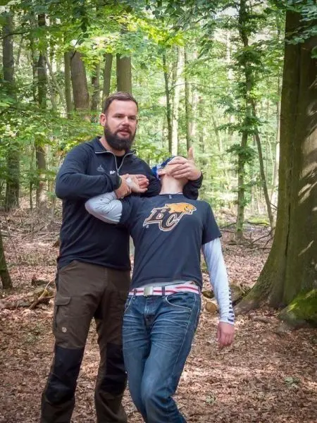 Person demonstriert eine Technik zur Kontrolle einer anderen Person im Wald