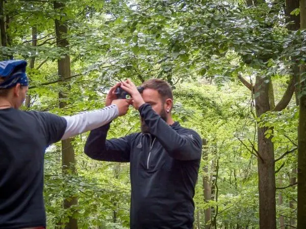 Person hält ein Gerät über den Kopf einer anderen Person im Wald