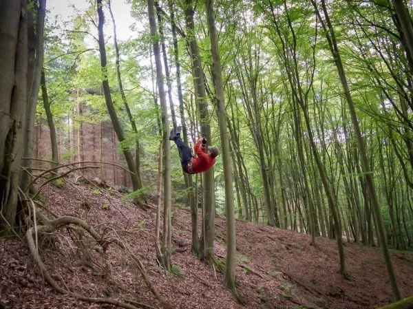Person hängt an einem Seil zwischen Bäumen im Wald