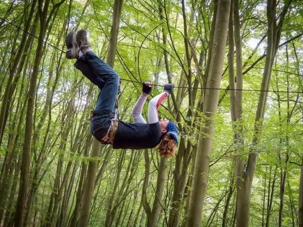 Person hängt kopfüber an einer Seilquerung zwischen Bäumen