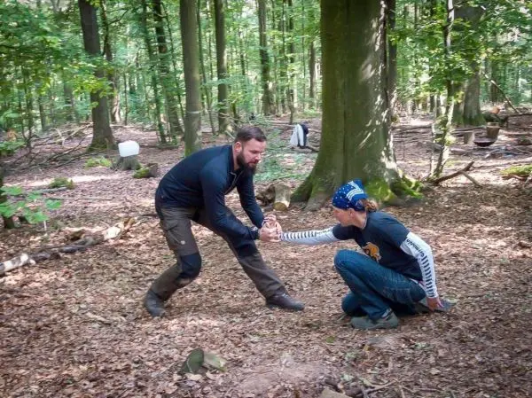 Person hilft anderer Person beim Aufstehen im Wald