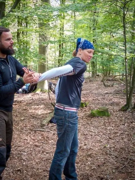 Person hilft anderer Person beim Üben einer Technik im Wald