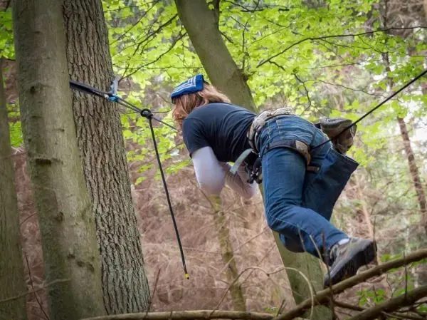 Person klettert mit Kletterausrüstung an einem Baumstamm hoch