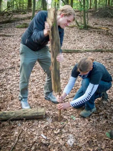 Person schlägt mit einem Stock auf einen anderen Stock im Wald