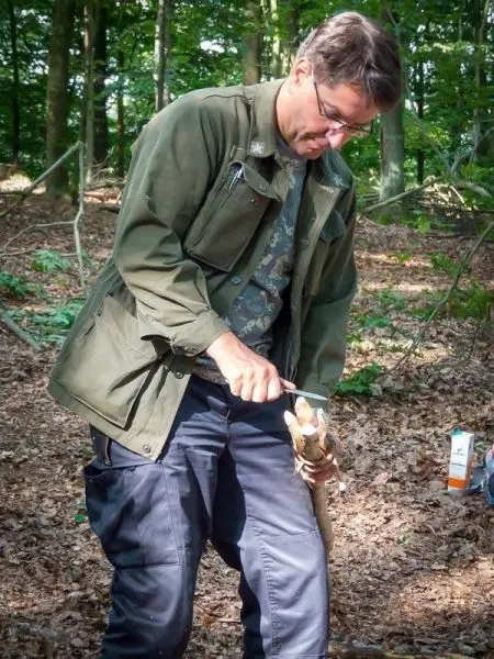 Person schnitzt mit einem Messer an einem Stock im Wald