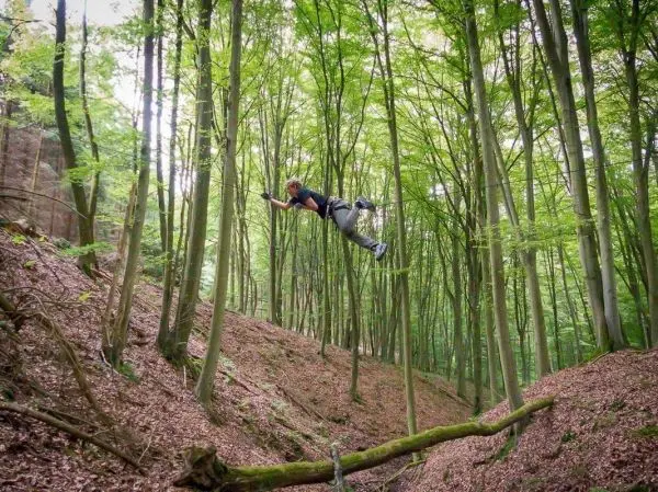 Person springt über einen Baumstamm im Wald