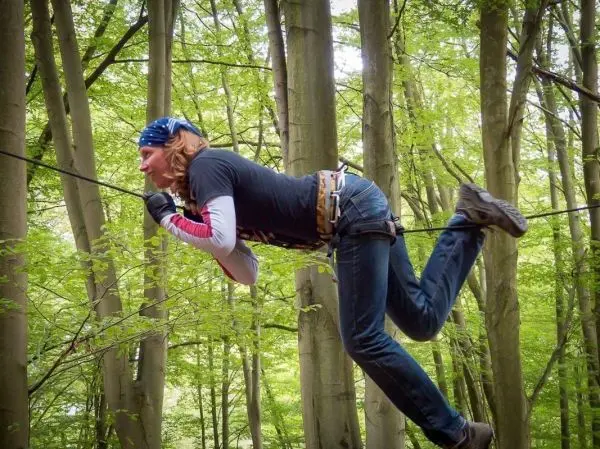 Person überquert eine selbstgebaute Seilbrücke zwischen Bäumen