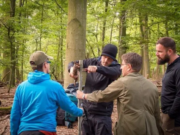 Person zeigt anderen Personen den Umgang mit einem Werkzeug im Wald