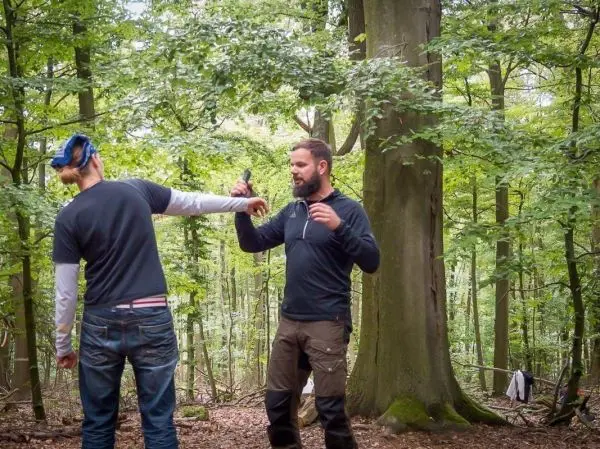 Person zeigt einer anderen Person eine Technik im Wald