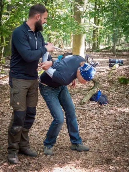 Person zeigt einer anderen Person eine Technik im Wald