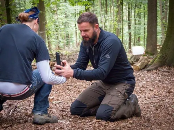 Person zeigt einer anderen Person eine Waffe im Wald