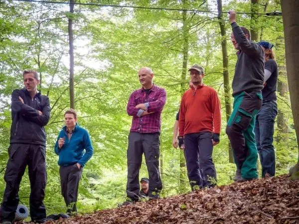 Sechs Personen stehen im Wald und beobachten eine Seilquerung