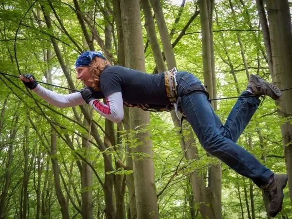 Selbstgebaute Seilquerung wird von einer Person in den Bäumen überquert