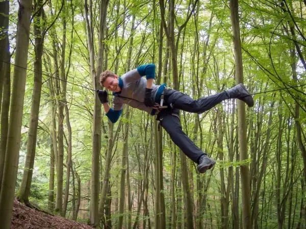 Überquert eine selbstgebaute Seilbrücke zwischen Bäumen im Wald