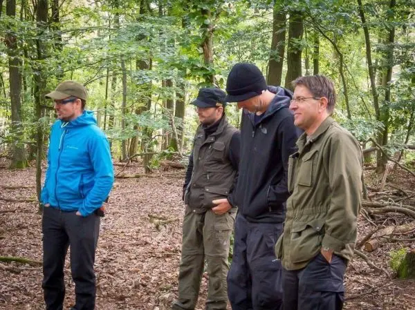 Vier Personen stehen im Wald und beobachten die Umgebung