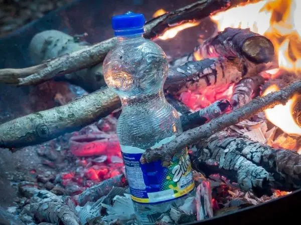 Wasserflasche steht zwischen brennenden Ästen im Feuer