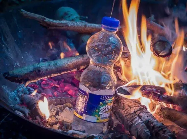 Wasserflasche steht zwischen brennenden Holzstücken
