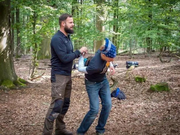 Zwei Personen in einem Wald, eine Person hält die andere am Handgelenk