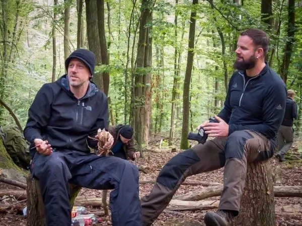 Zwei Personen sitzen auf Baumstümpfen im Wald und unterhalten sich