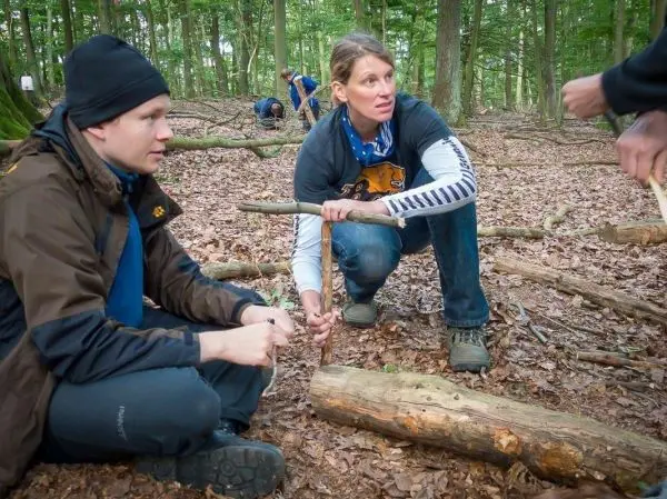 Zwei Personen sitzen im Wald und bearbeiten einen Holzstock mit einem Messer