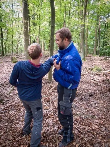 Zwei Personen stehen im Wald und sprechen miteinander