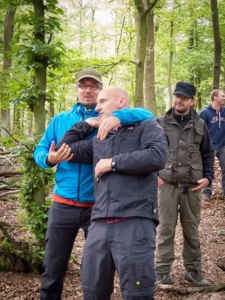 Zwei Personen stehen in einem Wald, eine Person umarmt die andere