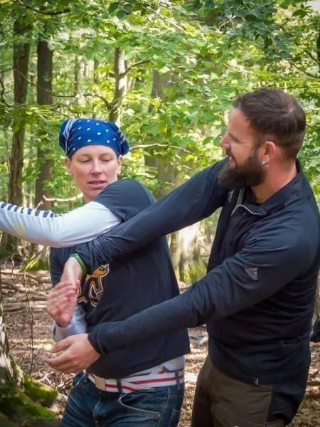 Zwei Personen üben eine Selbstverteidigungstechnik im Wald aus
