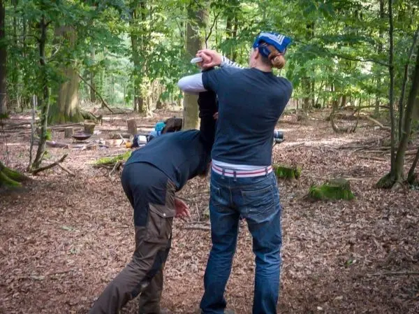 Zwei Personen üben eine Technik im Wald, einer hält den anderen am Arm