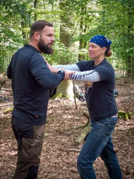 Zwei Personen üben eine Technik im Wald, Hände sind miteinander verbunden