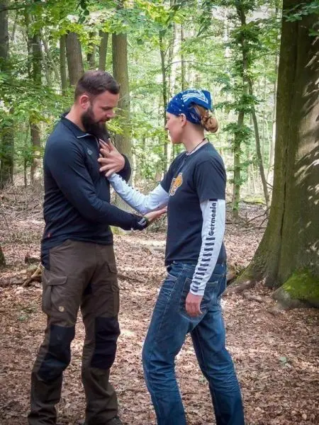 Zwei Personen üben eine Technik zur Selbstverteidigung im Wald