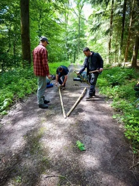 Drei Personen arbeiten an einer selbstgebauten Konstruktion aus Holzstöcken im Wald