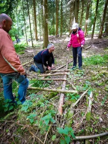 Drei Personen bauen eine selbstgebaute Konstruktion aus Ästen im Wald
