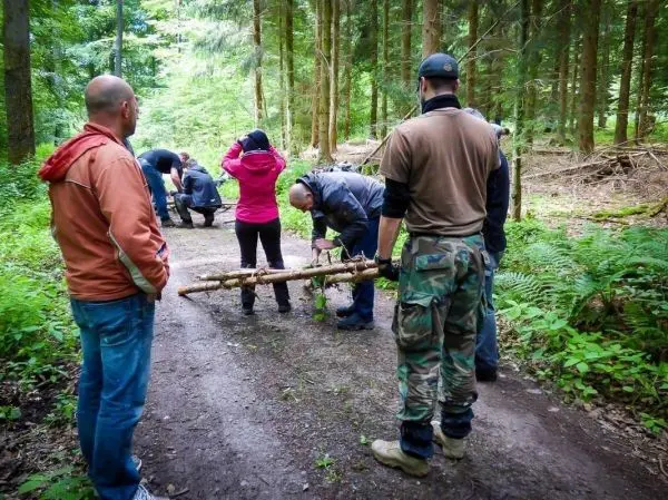 Gruppe arbeitet an einer improvisierten Trage aus Ästen im Wald