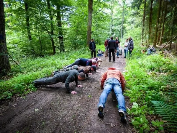 Gruppenteilnehmer führen Liegestütze auf einem Waldweg durch, umgeben von Bäumen und Grün