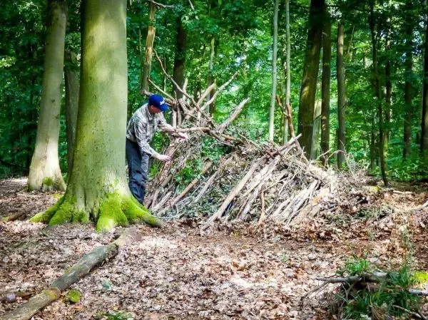 Mann baut eine Laubhütte aus Ästen und Zweigen im Wald