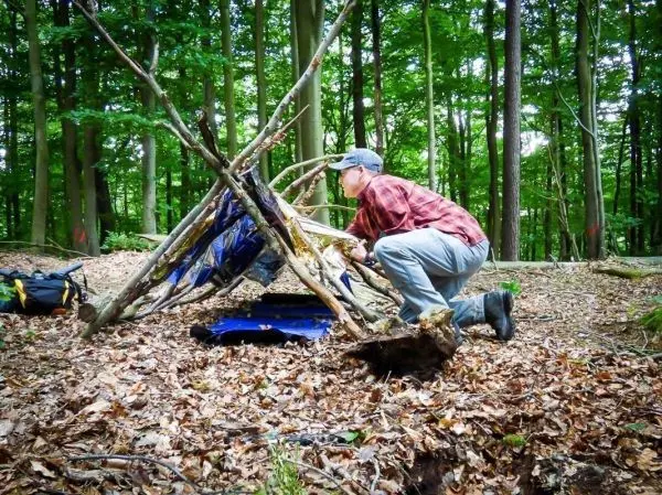 Mann baut eine Tarp-Notunterkunft aus Ästen und einer Plane im Wald