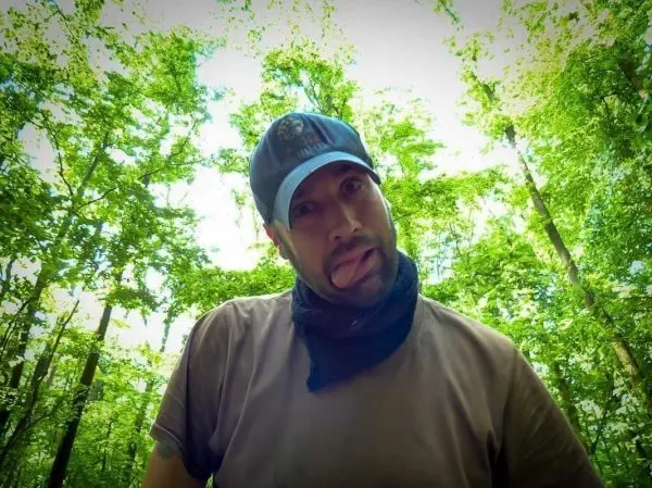 Person mit Mütze und Halstuch steht im Wald