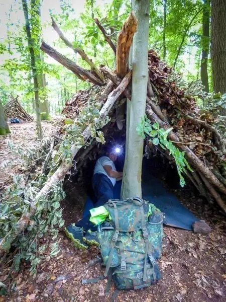 Person sitzt in selbstgebauter Unterkunft und hält Taschenlampe