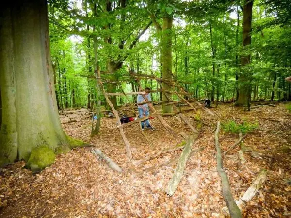 Person steht neben einer selbstgebauten Struktur aus Ästen im Wald