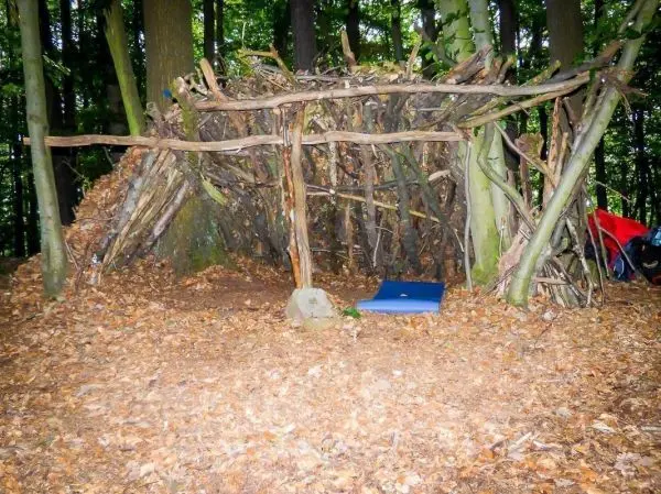 Selbstgebaute Laubhütte aus Ästen und Zweigen im Wald mit einer Matte im Inneren