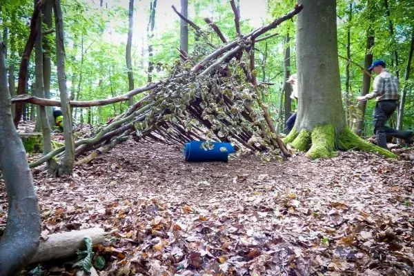 Selbstgebaute Tarp-Notunterkunft aus Ästen und Blättern im Wald