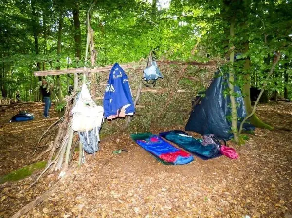 Selbstgebaute Tarp-Notunterkunft mit Schlafsäcken und Rucksäcken im Wald