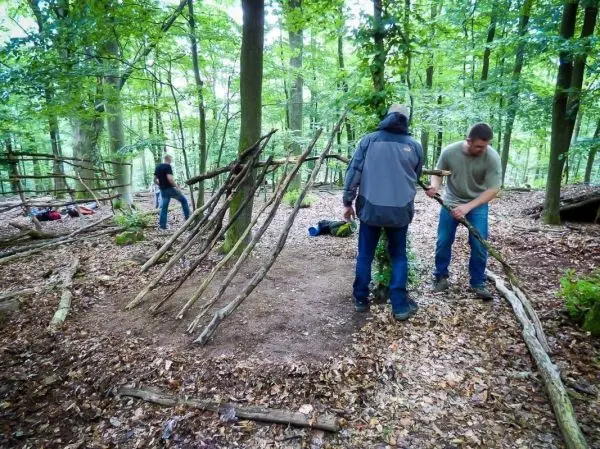 Zwei Personen bauen eine Holzstruktur im Wald, während eine weitere Person im Hintergrund arbeitet